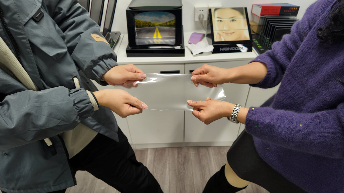 Hands demonstrating a transparent paint protection film sample